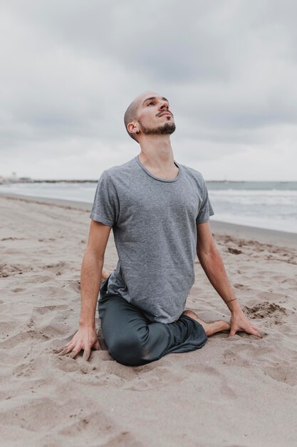 Hombre en la playa ejercitando posiciones de yoga