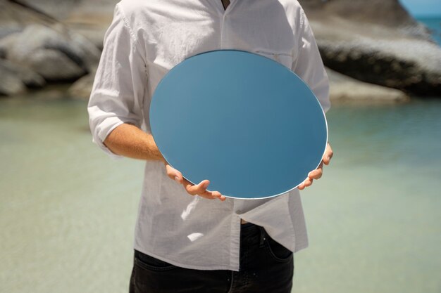 Hombre en la playa posando con espejo reflectante redondo