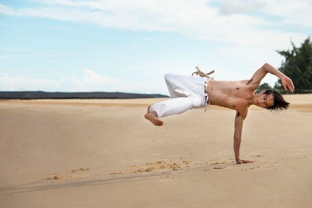 Foto gratuita hombre en la playa practicando capoeira solo