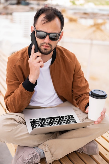 Hombre en la playa trabajando en la computadora portátil mientras toma un café