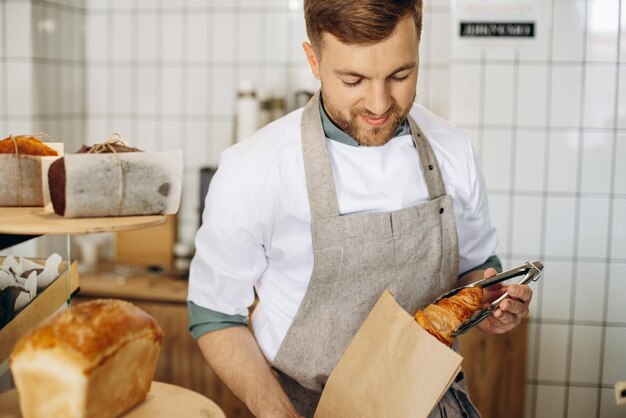 Hombre pone croissant en una bolsa de papel con pinzas