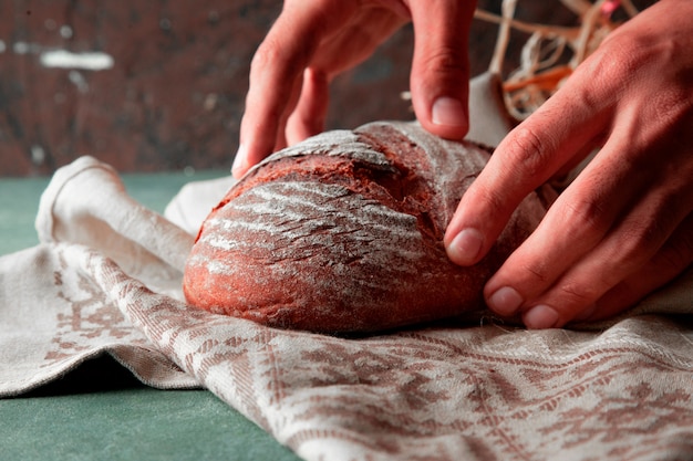 Hombre poner pan de trigo casero con harina sobre una toalla blanca con las dos manos.