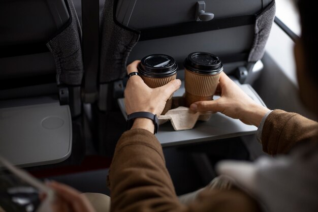 Hombre poniendo dos tazas de café en un asiento mientras viaja en tren
