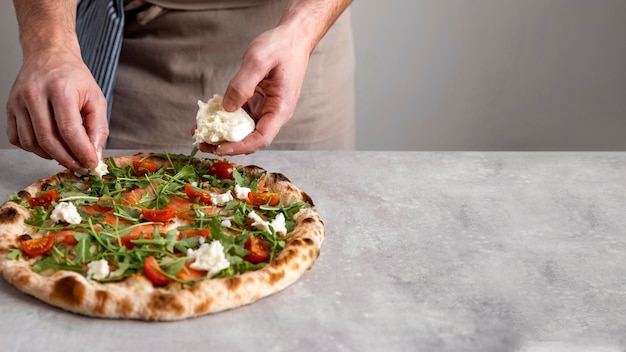 Hombre poniendo mozzarella sobre masa de pizza al horno con rodajas de salmón ahumado