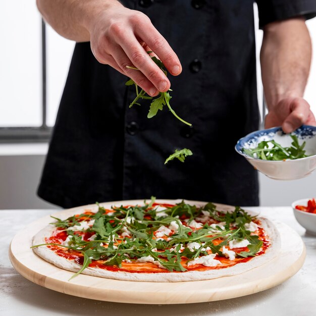 Hombre poniendo rúcula en masa para pizza