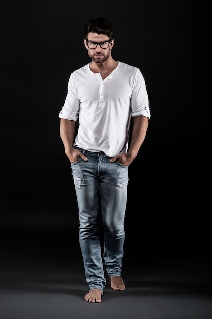 Hombre posando con anteojos, jeans y camiseta blanca.