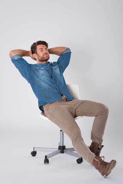 Hombre posando con camisa de mezclilla sentado en una silla