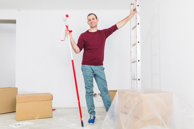 Hombre posando con escalera y rodillo de pintura