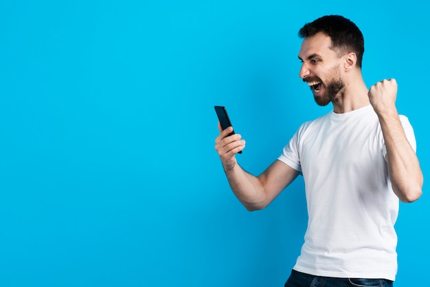 Hombre posando victorioso mientras sostiene el teléfono inteligente