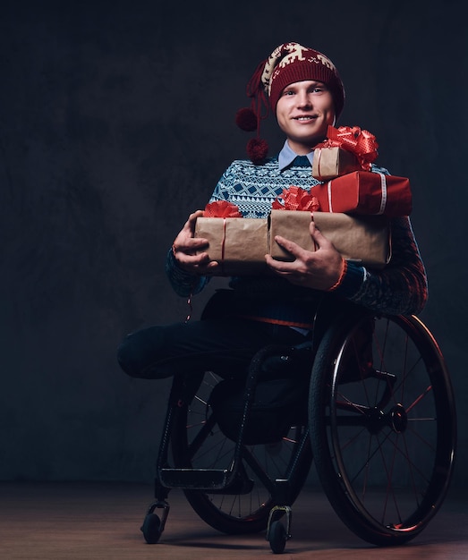 Foto gratuita hombre positivo en silla de ruedas con regalos de navidad sobre fondo gris oscuro.