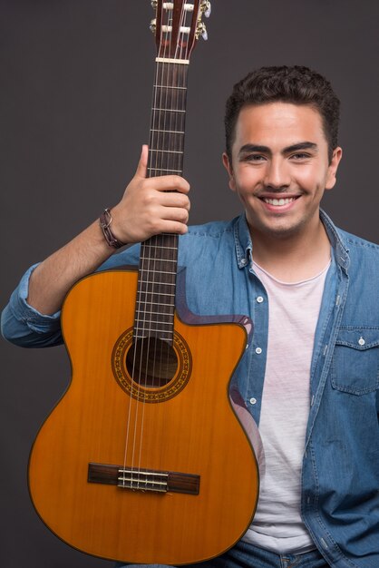 Hombre positivo sosteniendo una hermosa guitarra sobre fondo negro. Foto de alta calidad