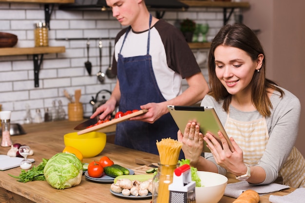 Hombre preparando ensalada mientras que mujer viendo tableta