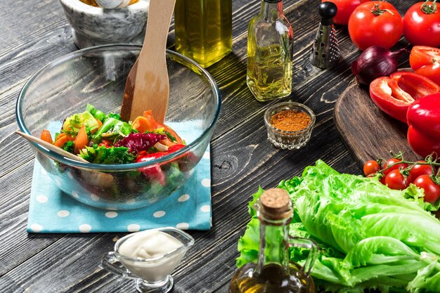 Hombre preparando ensalada con verduras frescas en una mesa de madera. Cocinar comida sabrosa y saludable. Sobre fondo negro. Comida vegetariana, saludable o concepto de cocina. De cerca