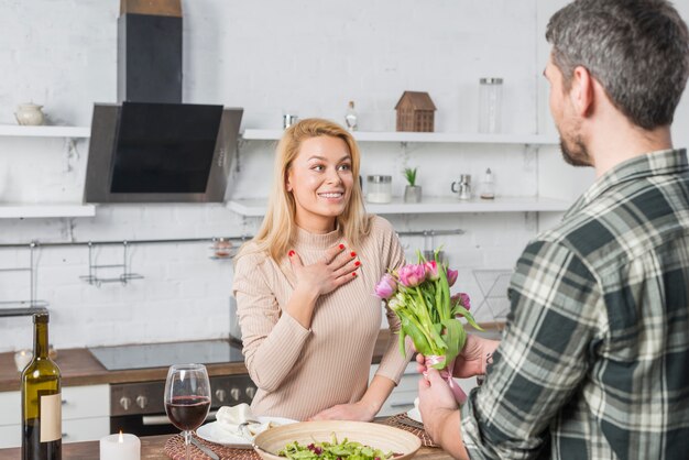 Hombre presentando flores a mujer sorprendida en cocina