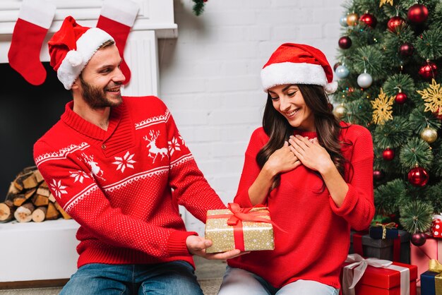 Hombre presentando regalo a mujer cerca de arbol de navidad