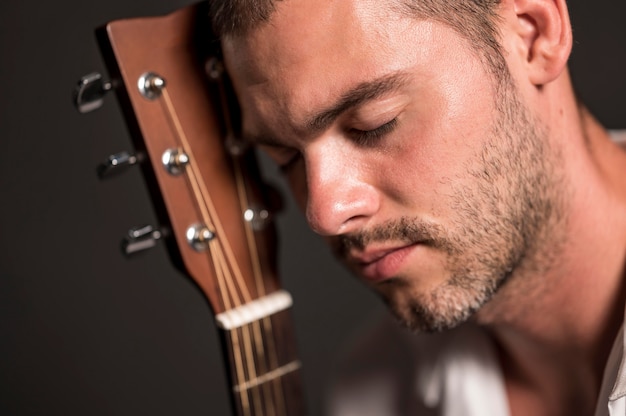 Hombre de primer plano sosteniendo su cabeza en el clavijero de guitarra