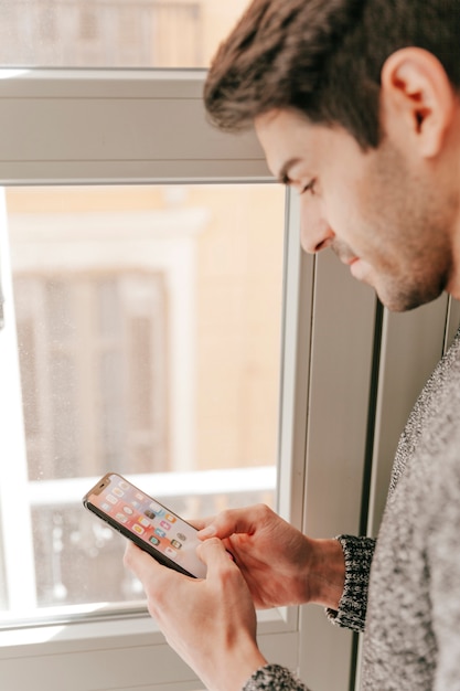 Hombre de primer plano con teléfono inteligente cerca de la ventana