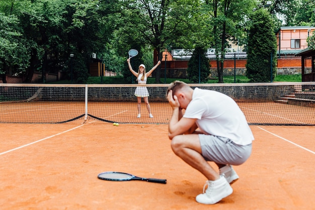 Hombre, profesor de tenis, mostrando a la mujer cómo jugar el deporte de raqueta al aire libre.