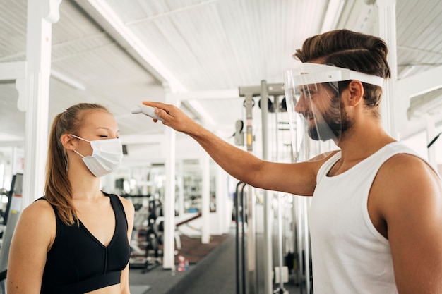 Foto gratuita hombre con protector facial comprobando la temperatura de la mujer en el gimnasio