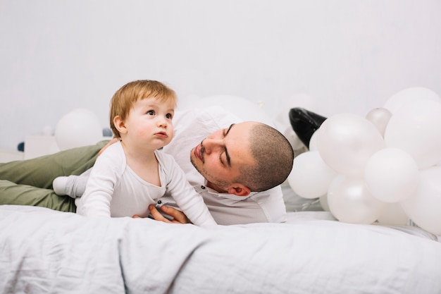 Hombre que abraza al pequeño bebé en cama cerca de los globos