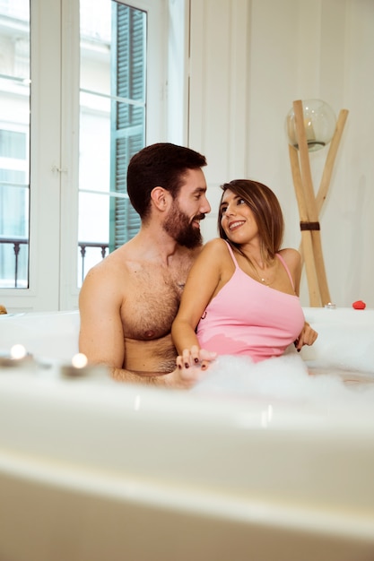 Hombre que abraza a la mujer sonriente en tina del balneario con agua y espuma