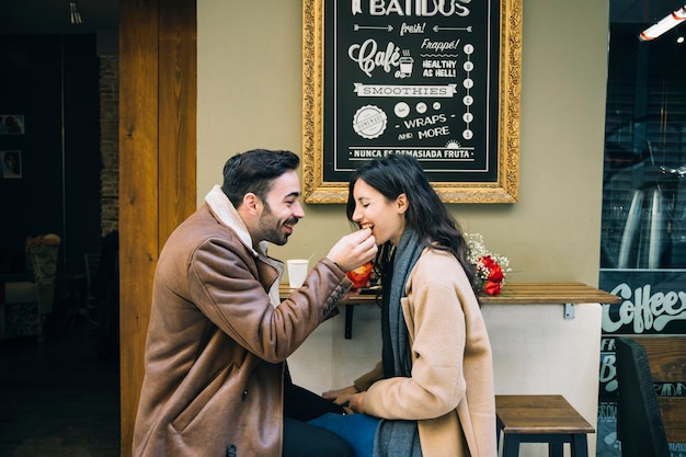 Hombre que alimenta a la mujer en el café al aire libre