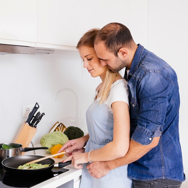 Hombre que ama a su esposa cocinando comida en la cocina de inducción en la cocina