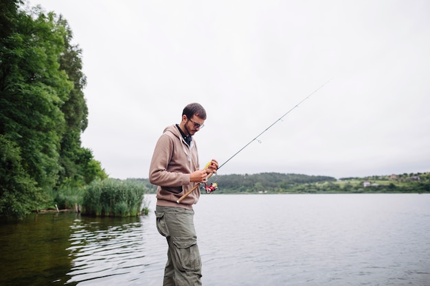 Hombre que ata el señuelo de la pesca en la barra cerca del lago