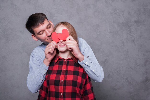 Hombre que cubre ojos de mujer con corazones de papel.