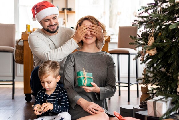Hombre que cubre los ojos de su esposa para una sorpresa navideña