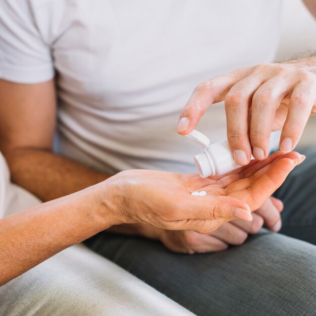 Hombre que da píldoras a la mano de la mujer mayor