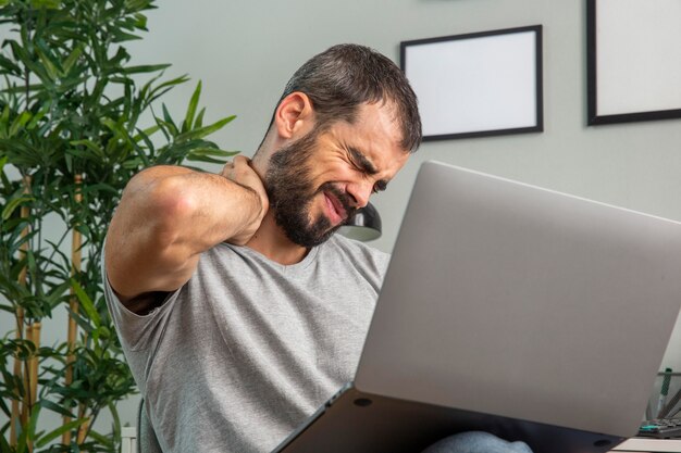 Hombre que experimenta dolor de cuello mientras trabaja desde casa en la computadora portátil