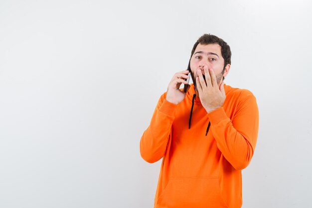 el hombre que habla móvil sorprende al cubrirse la boca con la mano en el fondo blanco