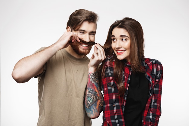 Foto gratuita hombre que hace caras divertidas que juegan con el pelo de la muchacha en blanco.