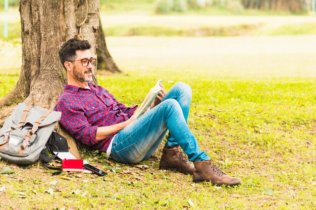 Hombre que se inclina debajo del árbol leyendo libros en el parque