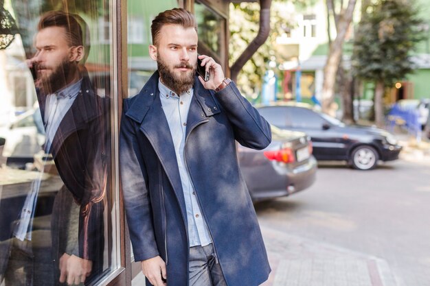 Hombre que se inclina en la ventana de cristal que habla en el teléfono celular