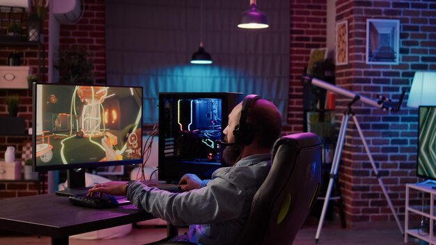 El hombre que juega en línea en el torneo de disparos en primera persona felicita al equipo por los auriculares después de celebrar la victoria en la PC de juegos en casa. Competición ganadora de jugadores profesionales haciendo el gesto de la mano de la victoria.