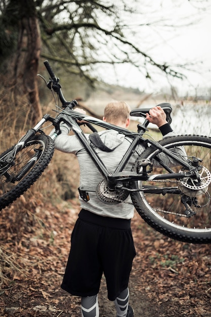 Hombre que lleva bicicleta deportiva en su espalda caminando en el bosque