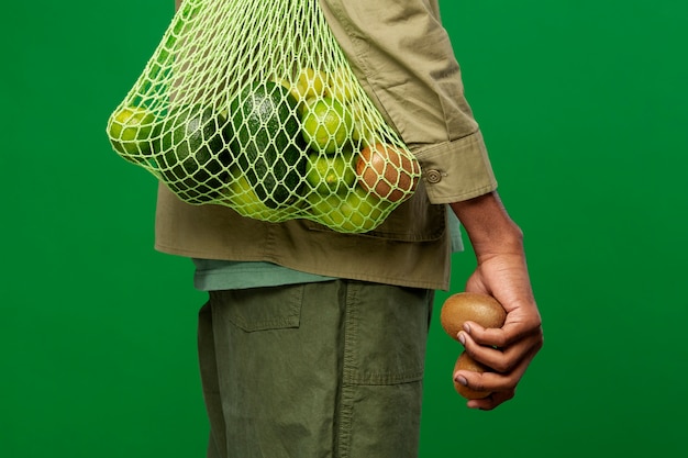 Foto gratuita hombre que lleva una bolsa de malla con fruta verde.