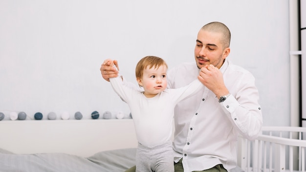 Foto gratuita hombre que lleva a cabo las manos del pequeño bebé divertido en cama