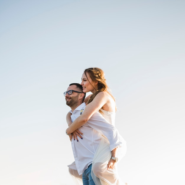 Hombre que lleva a su novia en su espalda en una playa contra el cielo azul