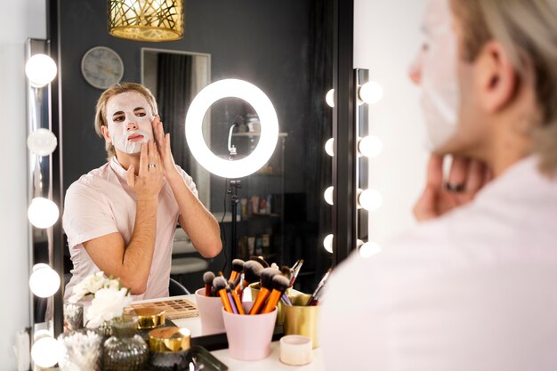 Hombre que llevaba maquillaje aplicando una máscara facial en el espejo