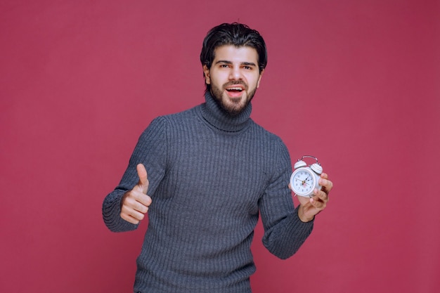 Hombre que muestra un reloj de alarma blanco y un punto de paking a una mejor oferta.