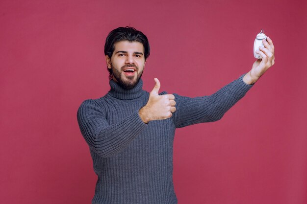 Hombre que muestra un reloj de alarma blanco y un punto de paking a una mejor oferta.