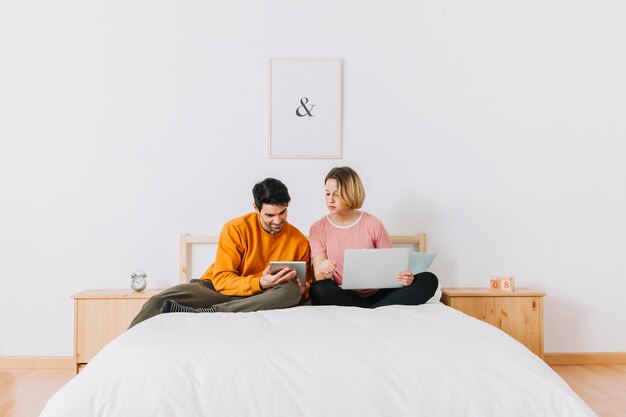 Hombre que muestra la tableta de la mujer en la cama