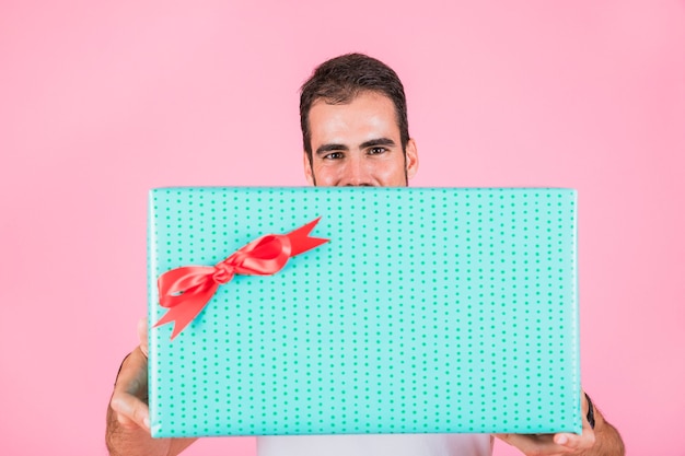 Foto gratuita hombre que ofrece la caja de regalo rectangular que se opone al contexto rosado