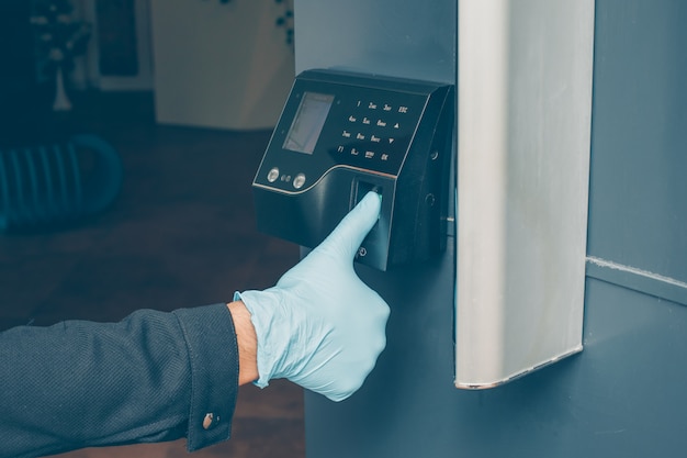 un hombre que recibe el intercomunicador para leer su huella digital para abrir la puerta con los guantes puestos.