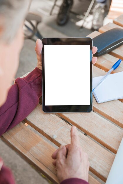 Hombre que señala el dedo hacia la tableta digital con pantalla en blanco en blanco en la mesa de madera