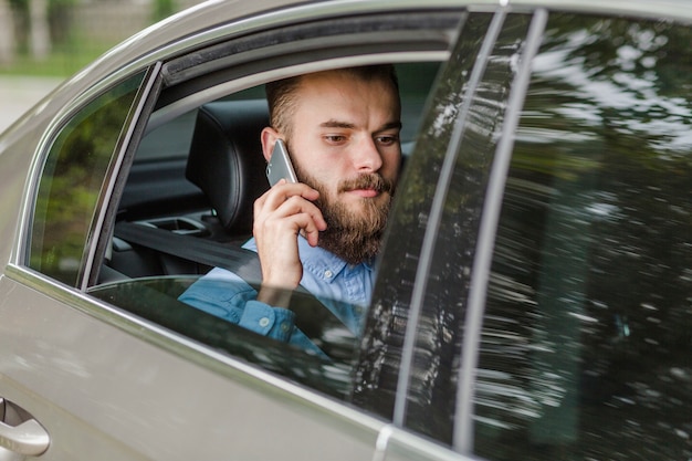 Foto gratuita hombre que se sienta dentro del coche usando el teléfono celular