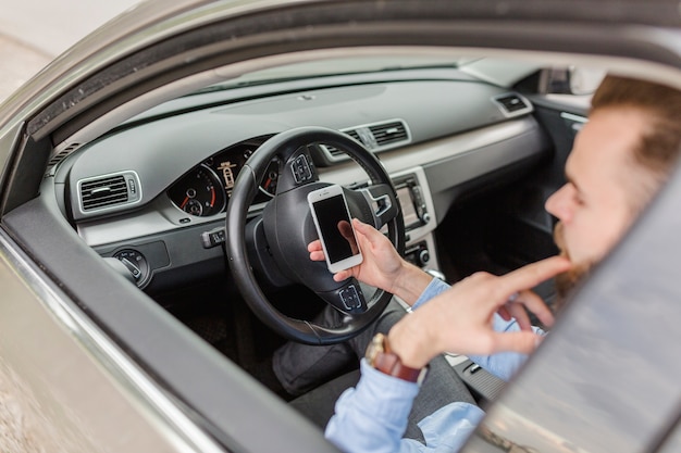 Hombre que se sienta dentro del coche usando el teléfono móvil